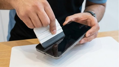 Person cleaning a smartphone screen with a cloth on a white surface.